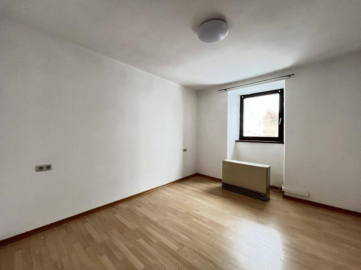 Heller, leerer Raum mit Laminatboden, einem Fenster und einem Heizkörper an der Wand.