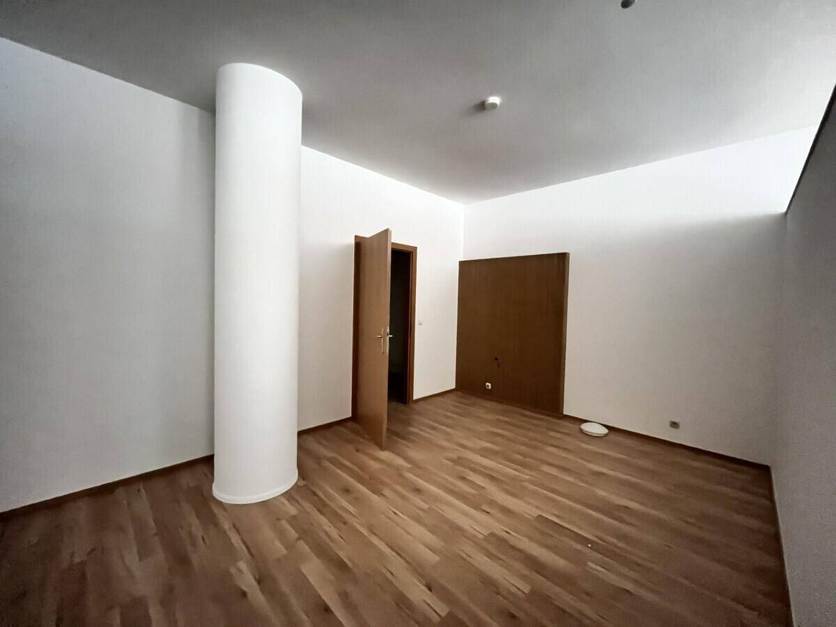 Leerer Raum mit Holzbodenoptik und einer zentralen Säule, ideal als Schlaf- oder Arbeitszimmer.
