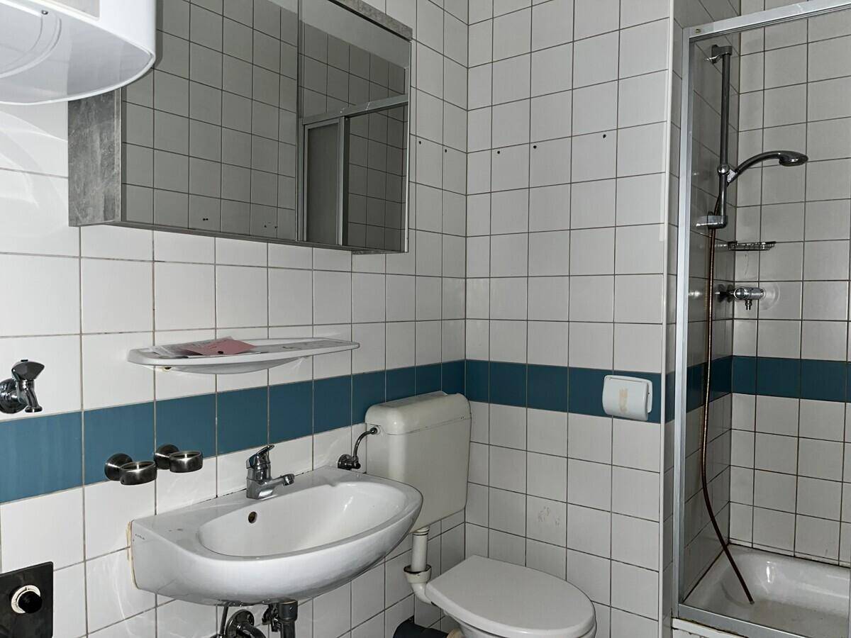 Badezimmer mit weißen und blauen Fliesen, Dusche, Waschbecken und Spiegelschrank.