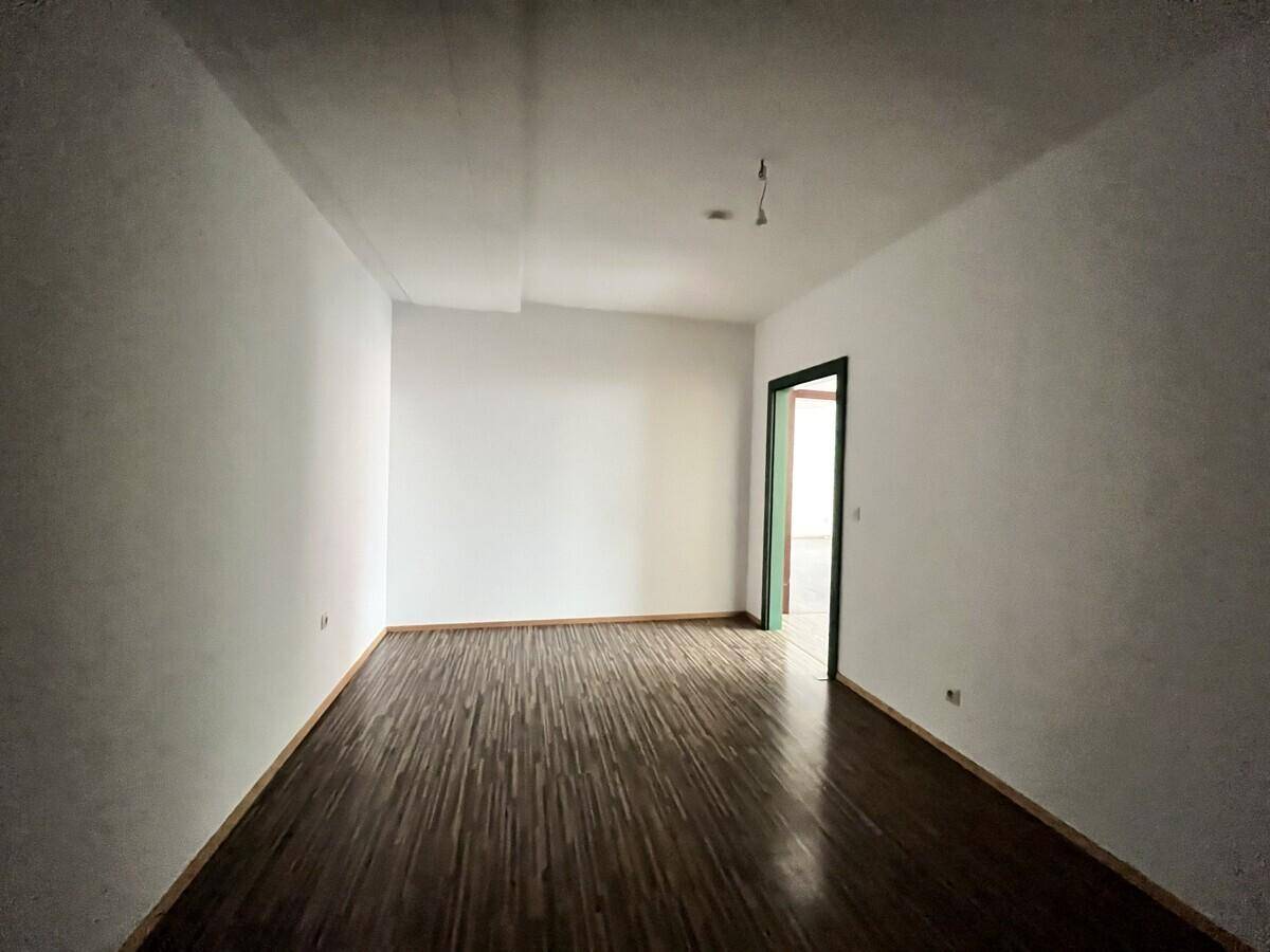 Leerer Raum mit dunklem Holzboden, weißen Wänden und einer grünen Tür.