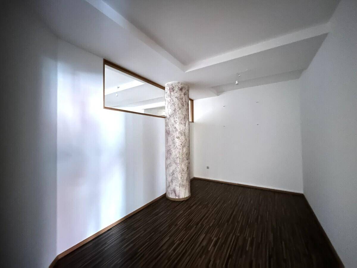 Heller Flur mit dunklem Holzboden, weiß gestrichenen Wänden und einer Marmorsäule.
