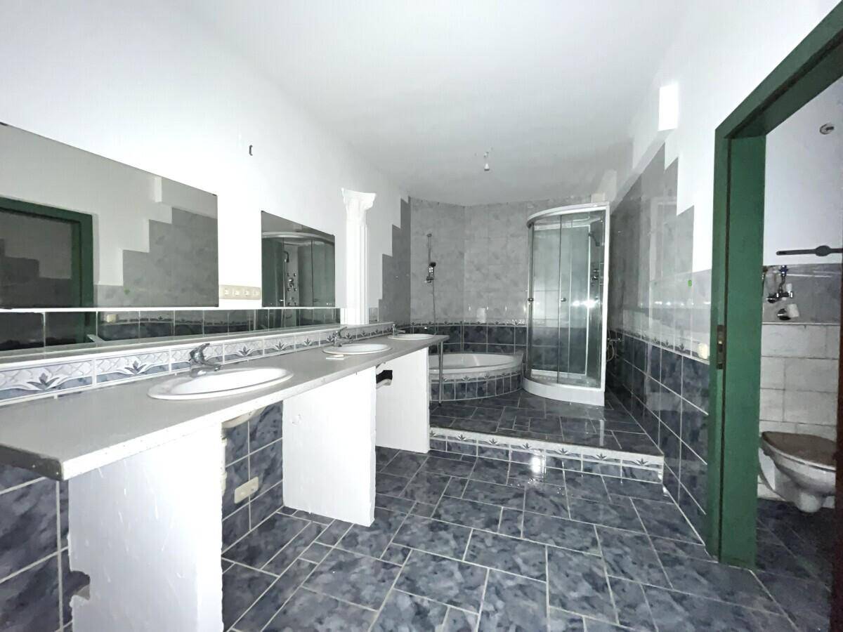 Geräumiges Badezimmer mit Doppelwaschbecken, Dusche, Badewanne und blaugrauen Fliesen.