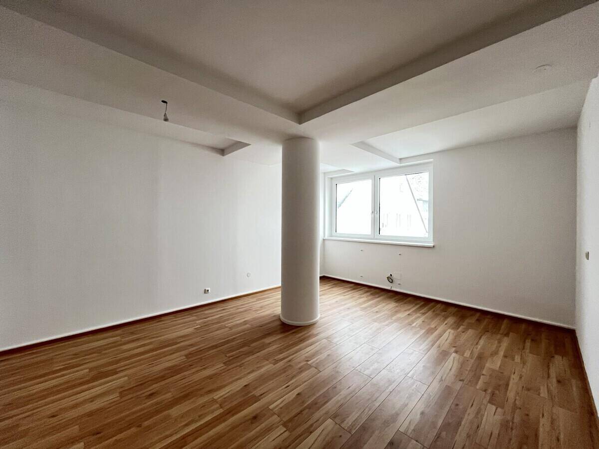 Heller, leerer Raum mit Holzboden, weiß gestrichenen Wänden und einem Fenster.