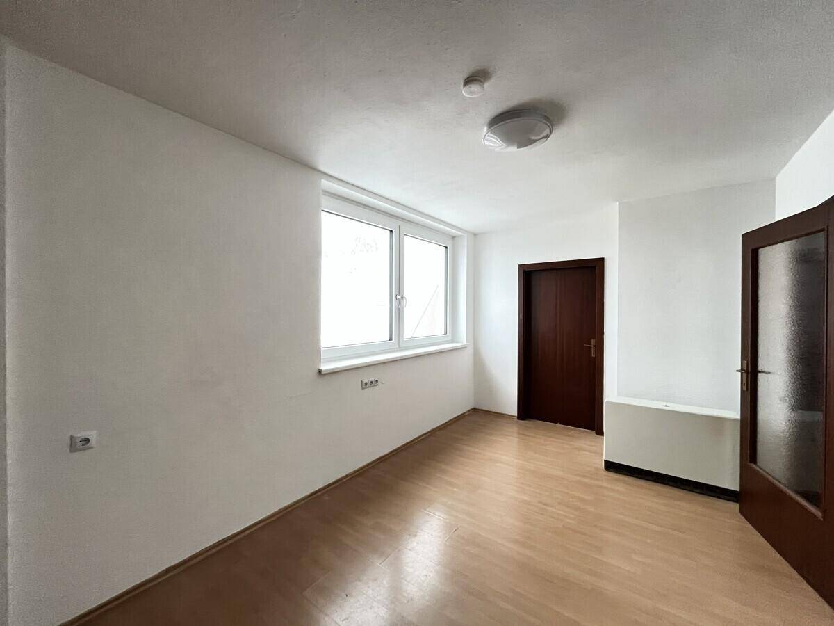 Leeres Schlafzimmer mit hellem Parkettboden und einem Fenster.