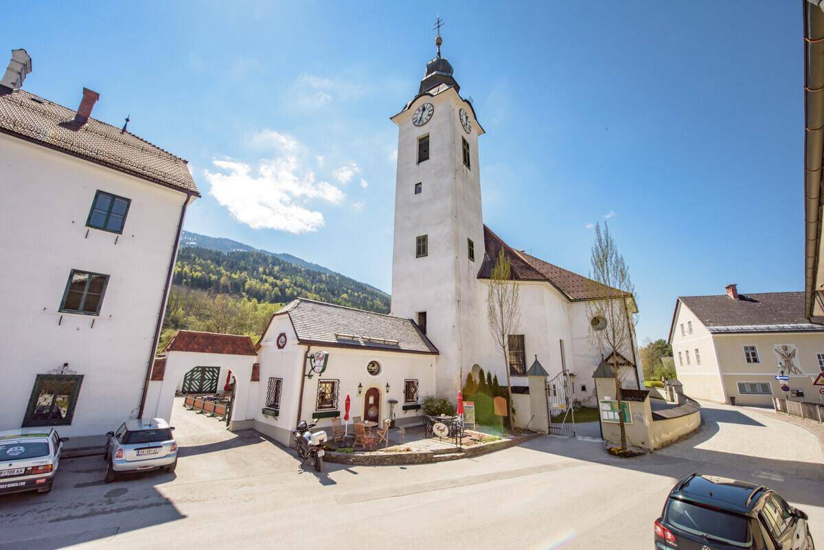 Historische Kirche mit Uhrturm und umliegenden Gebäuden in einem sonnigen Dorf.