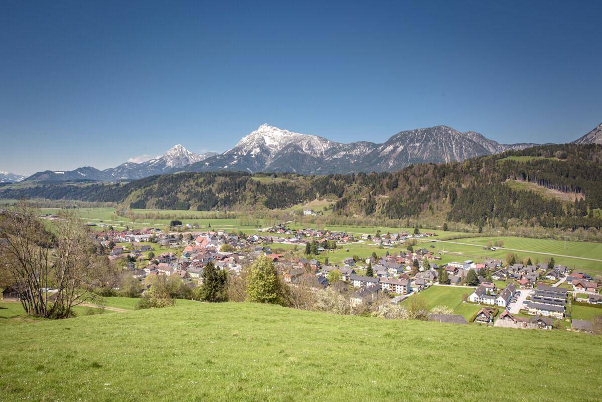 Weitläufiger Blick auf ein idyllisches Dorf in einem grünen Tal umgeben von Bergen.
