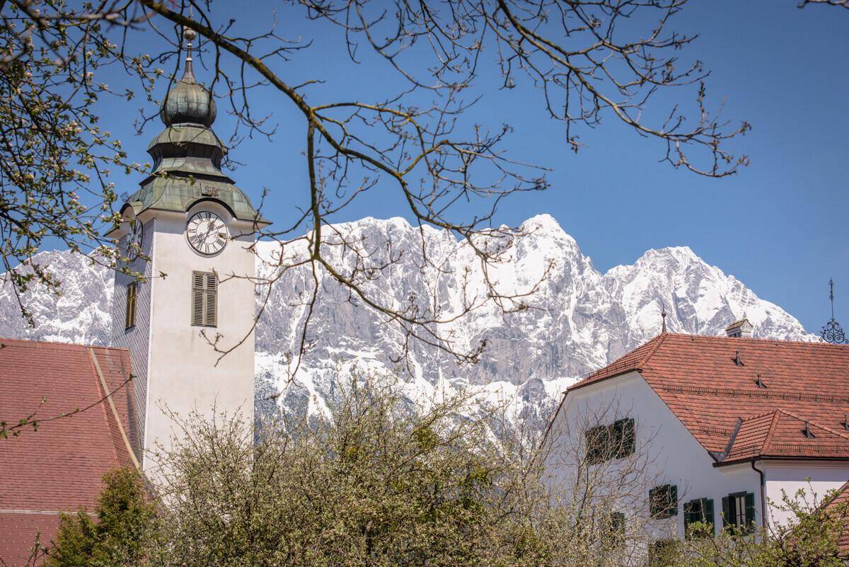 Kirchturm mit Uhr vor einer beeindruckenden Kulisse schneebedeckter Berge.
