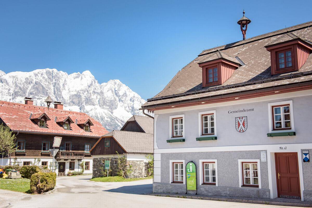 Traditionelle Gebäude in einem Dorf mit schneebedeckten Bergen im Hintergrund unter blauem Himmel.