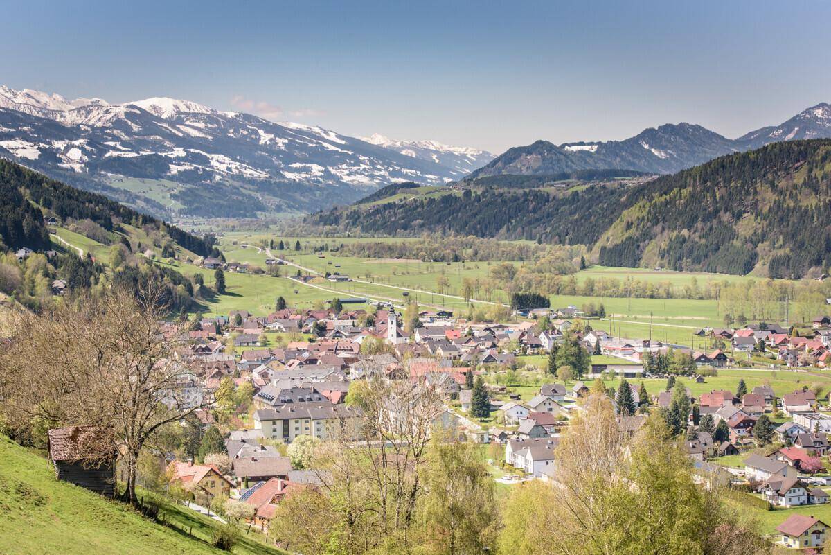 Panoramablick auf ein alpines Dorf mit schneebedeckten Bergen im Hintergrund.