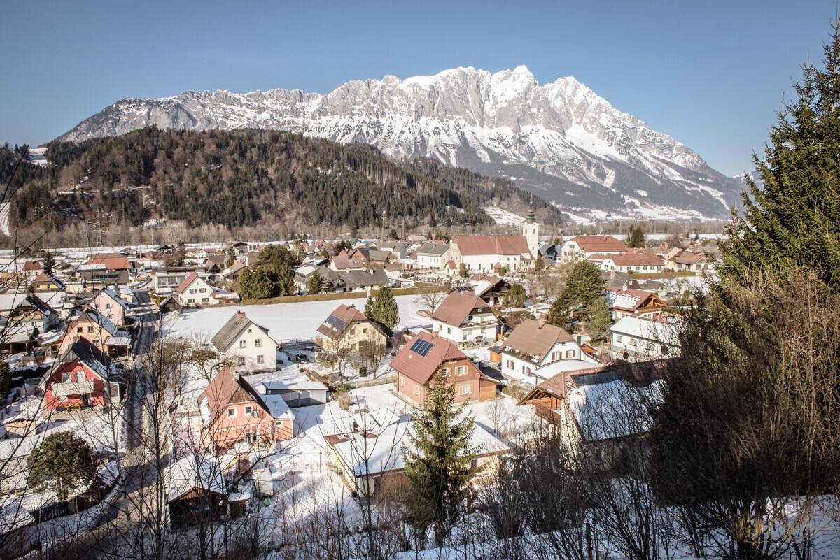 Winterlandschaft mit verschneitem Dorf und imposanten Bergen unter blauem Himmel.