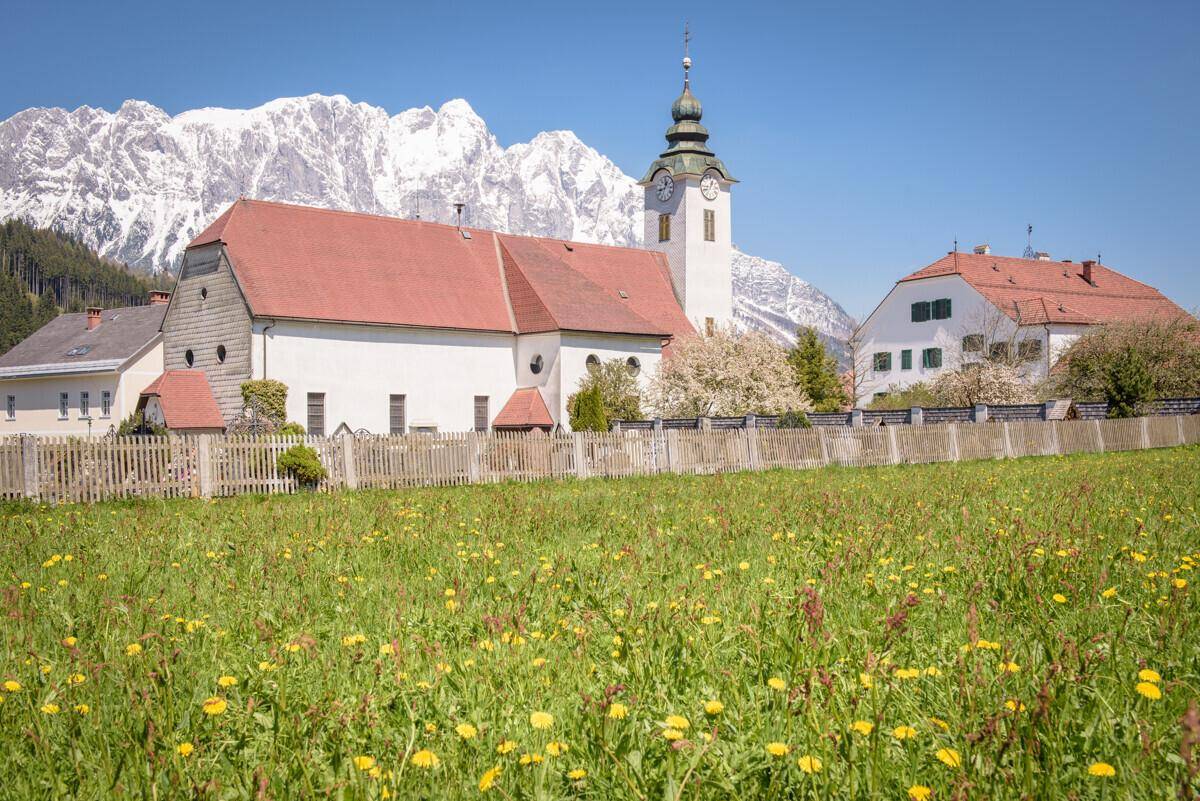 Kirche mit rotem Dach und Bergblick, umgeben von einer grünen Wiese.
