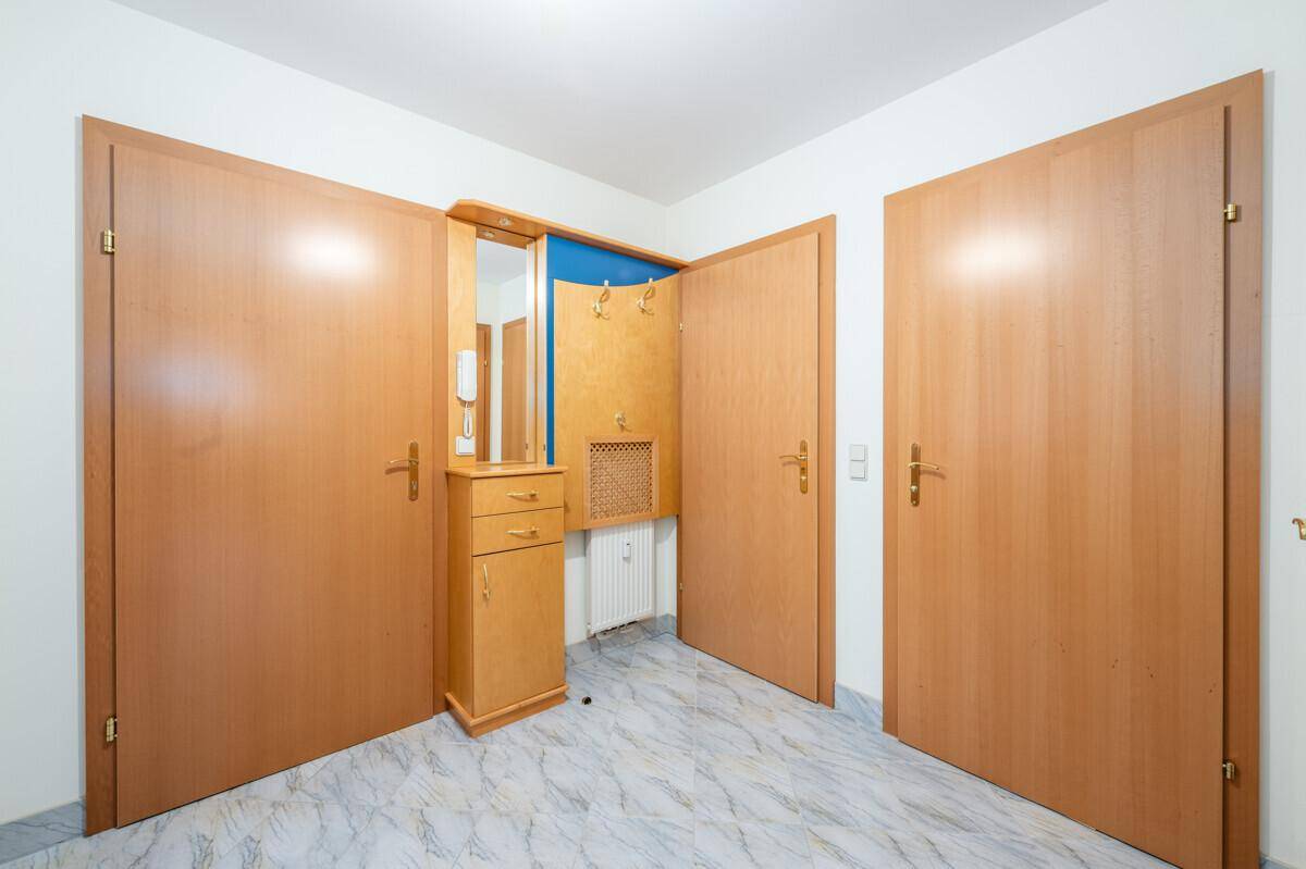 Eingangsbereich mit gefliestem Boden, Garderobe und Spiegel, umgeben von Holztüren.