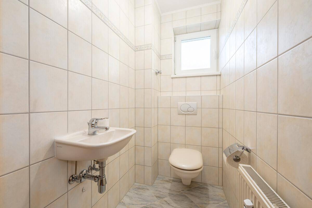Separates Gäste-WC mit Wand-WC, kleinem Waschbecken und Fenster für Tageslicht.