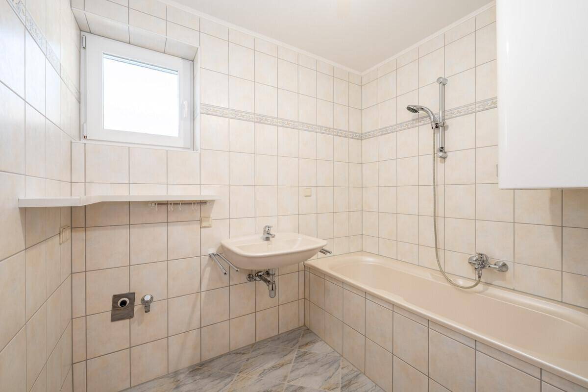 Gefliestes Badezimmer mit Badewanne, Waschbecken und Fenster für gute Belüftung.