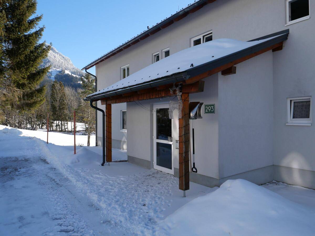 Eingangsbereich eines Gebäudes im Winter mit Schnee und einer überdachten Veranda.