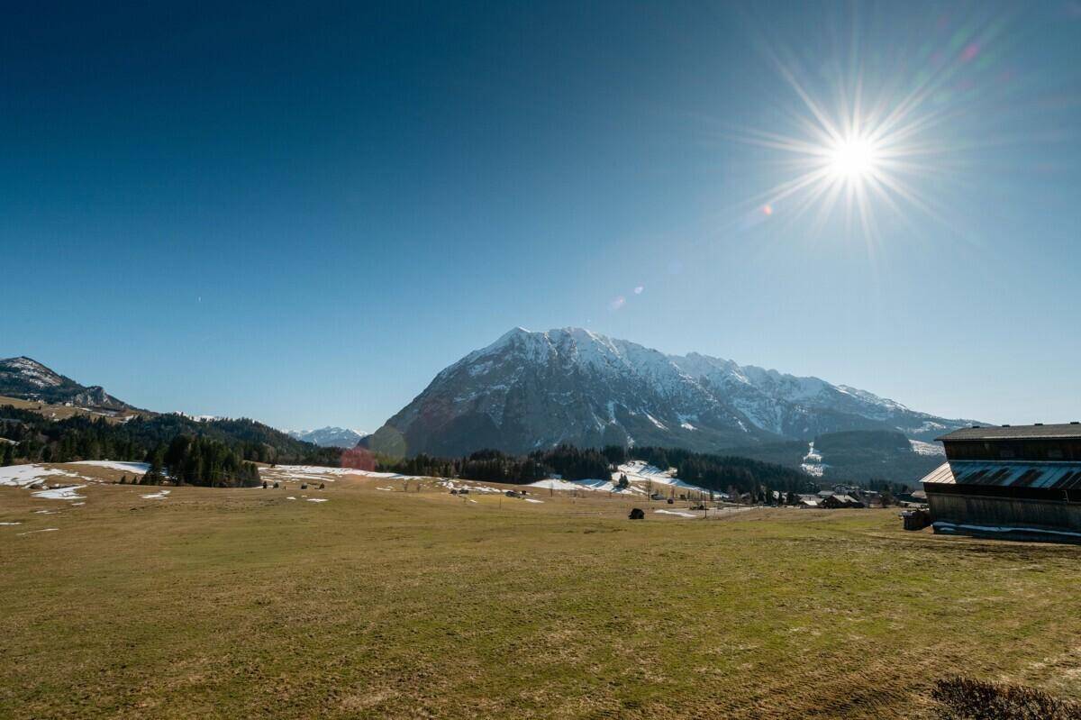 Weitläufige Landschaft mit schneebedeckten Bergen und grünen Wiesen unter strahlend blauem Himmel.