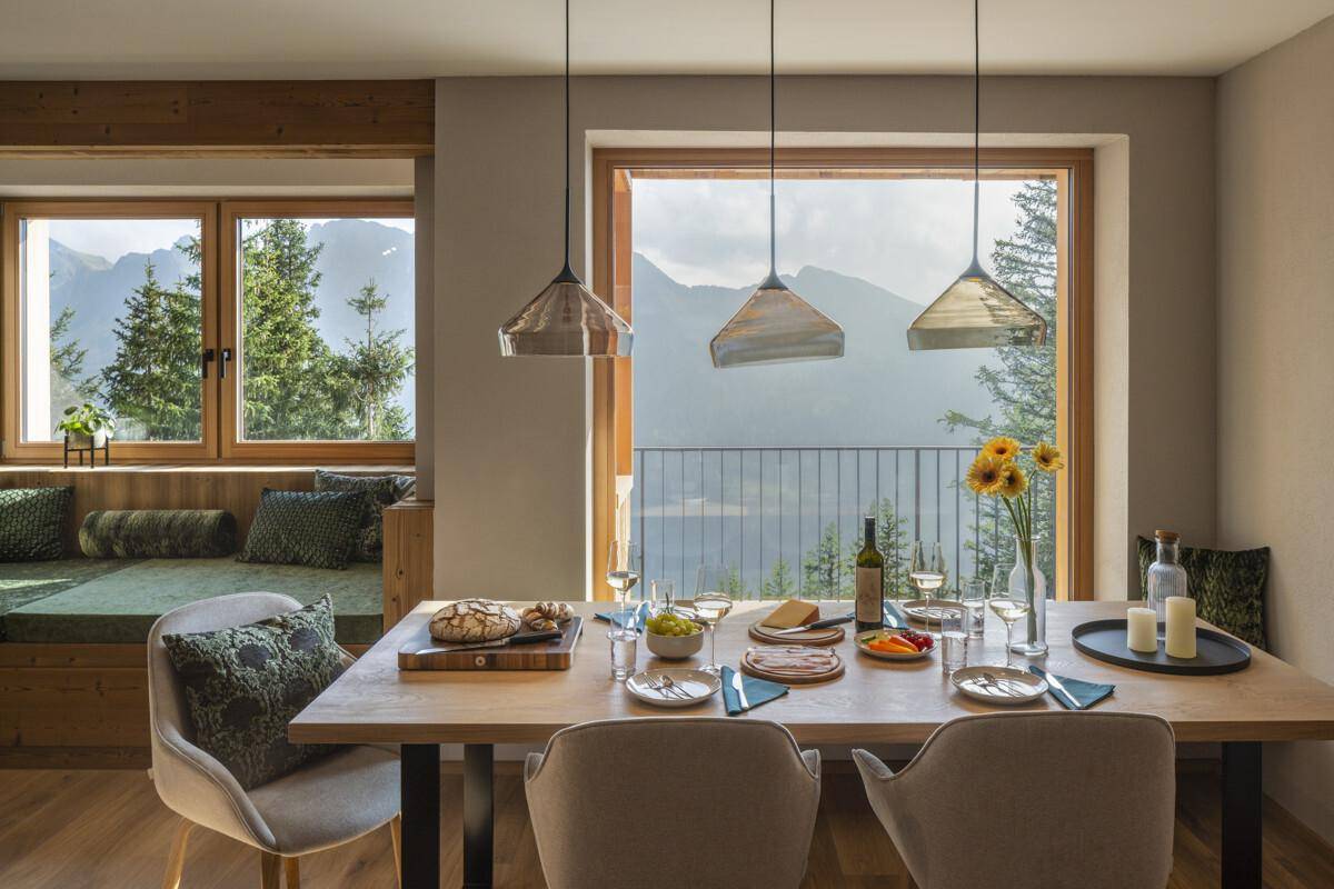 Heller Essbereich mit Holztisch, Sitzbank und großen Fenstern mit beeindruckendem Bergblick.