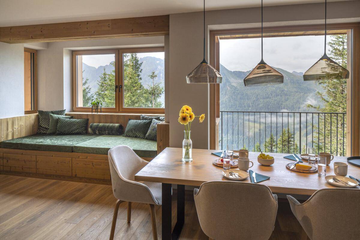Heller Essbereich mit Holztisch, Sitzbank und großen Fenstern mit beeindruckendem Bergblick.