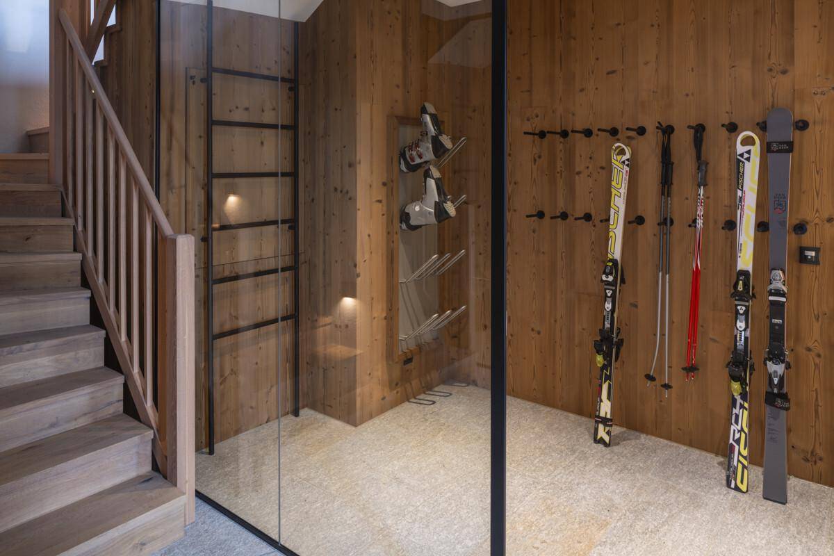Moderner Skiraum mit Holzverkleidung, Skihaltern und Stiefeltrocknern neben einer Treppe.