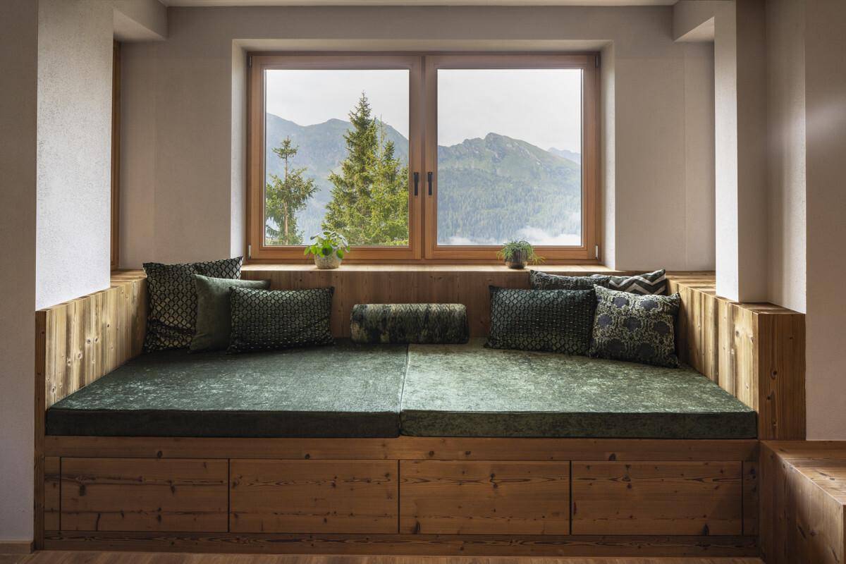 Gemütliche Sitzbank am Fenster mit grünen Kissen und weitem Blick auf die umliegende Berglandschaft.