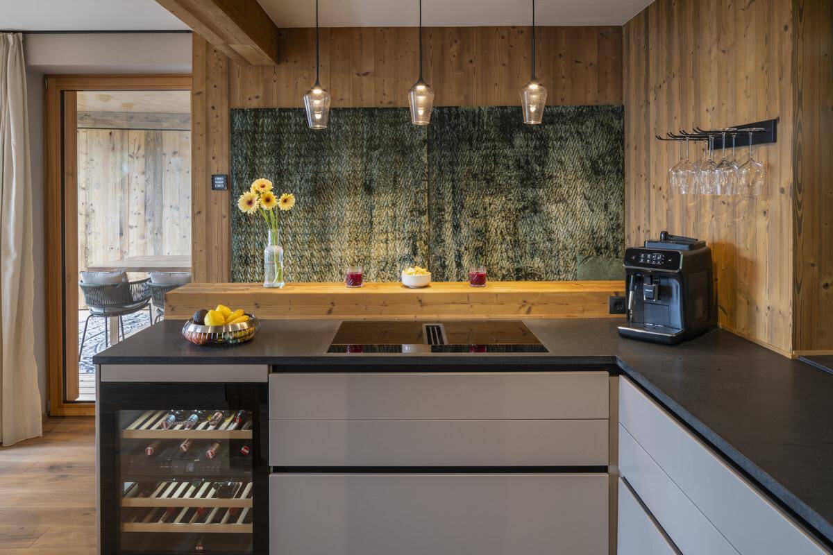 Moderne Küche mit Induktionskochfeld, Kaffeemaschine, Weinkühler und Holzverkleidung.