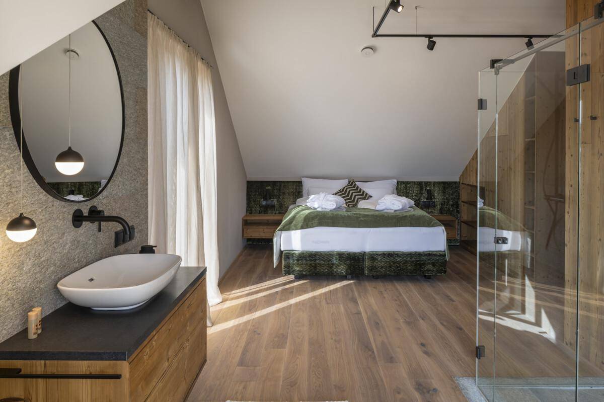 Schlafzimmer mit angeschlossenem Badbereich, Holzboden und schräger Decke unter dem Dach.