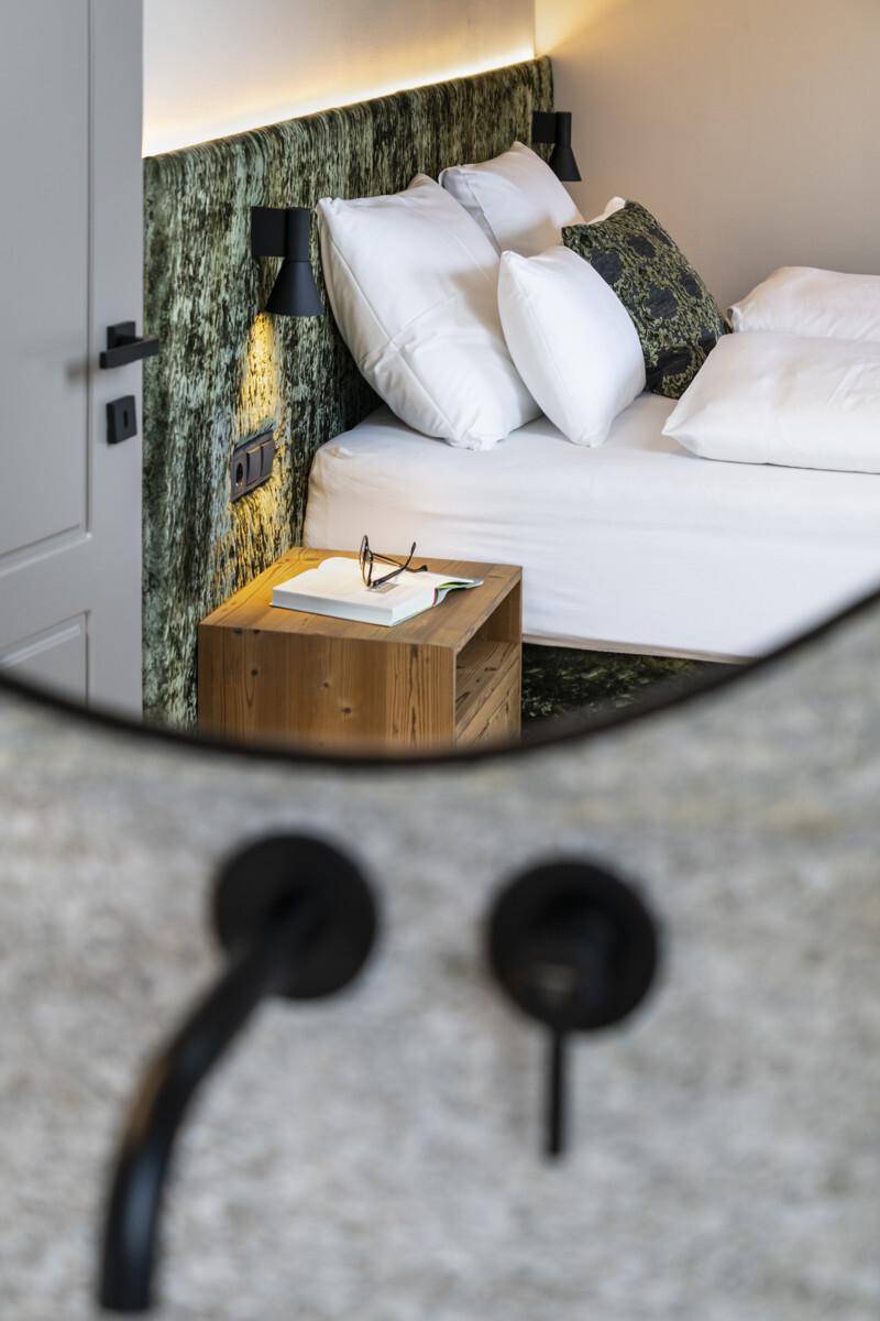 Detailansicht des Schlafzimmers mit Nachttisch, Leselampe und reflektiertem Spiegelbild.