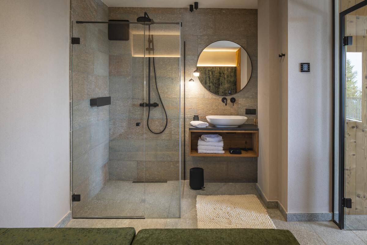 Modernes Badezimmer mit begehbarer Dusche, Waschtisch und runden Spiegel.