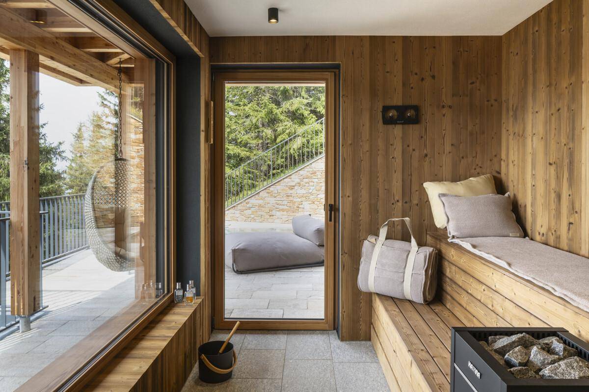 Moderne Sauna mit Holzbänken, Saunaofen und Blick auf eine Außenterrasse.