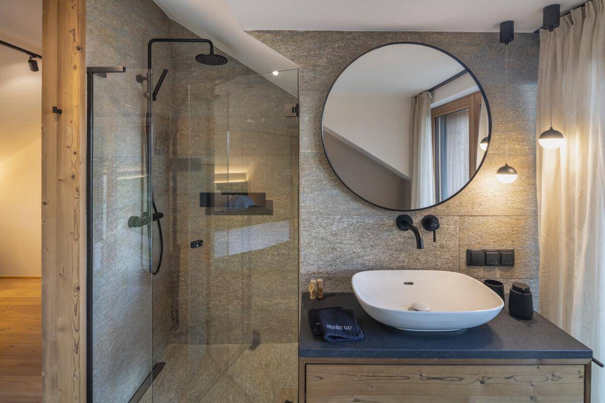 Stilvolles Badezimmer mit begehbarer Dusche, modernem Waschtisch und großem Rundspiegel.