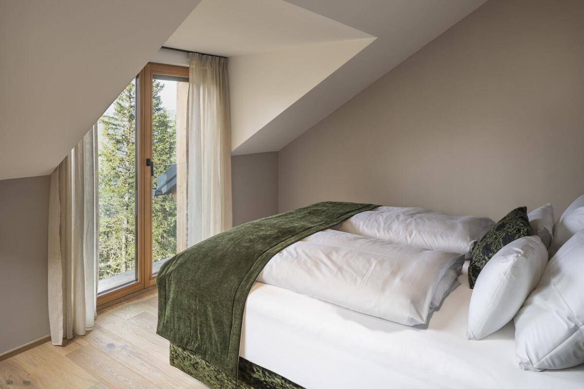 Gemütliches Schlafzimmer mit großem Bett, grüner Decke und einem Fenster mit Bergblick.