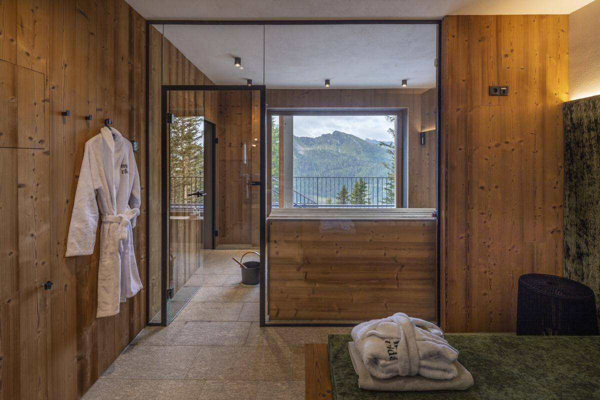 Gemütlicher Wellnessbereich mit Bademänteln, Holzwänden und einem Fenster mit Bergblick.