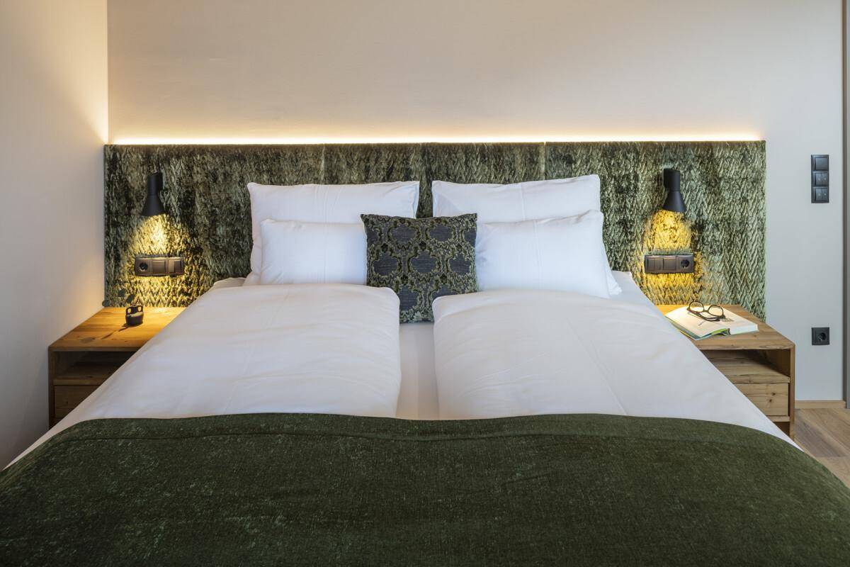 Komfortables Schlafzimmer mit großem Doppelbett, grüner Kopfstütze und indirekter Beleuchtung.