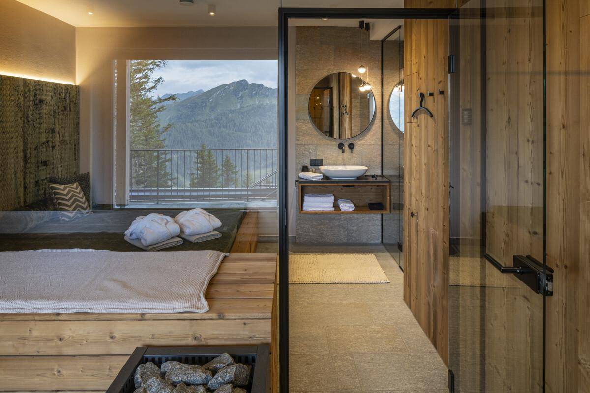 Wellnessbereich mit Sauna, Blick auf das Badezimmer und die beeindruckende Berglandschaft.