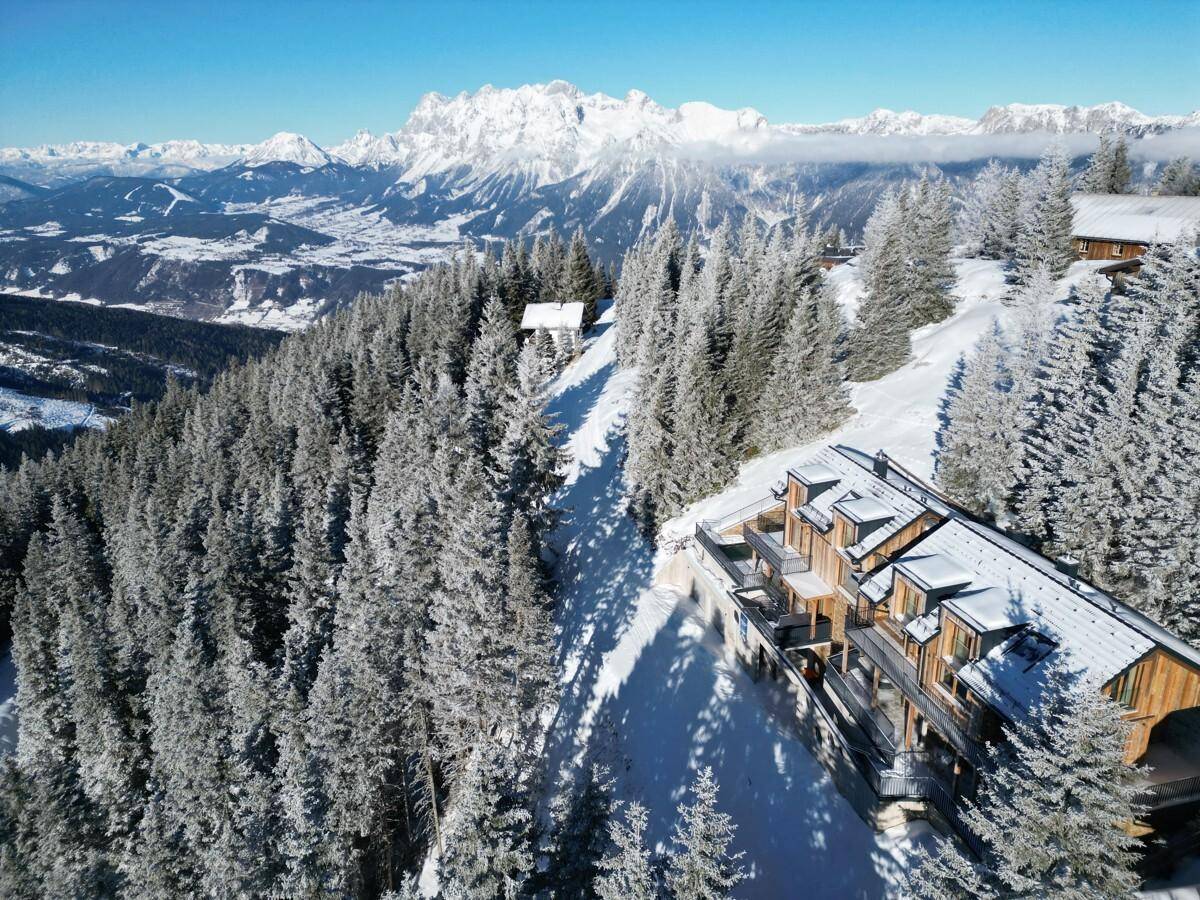 Atemberaubende Luftaufnahme eines Chalets in den verschneiten Alpen mit weitem Bergblick.