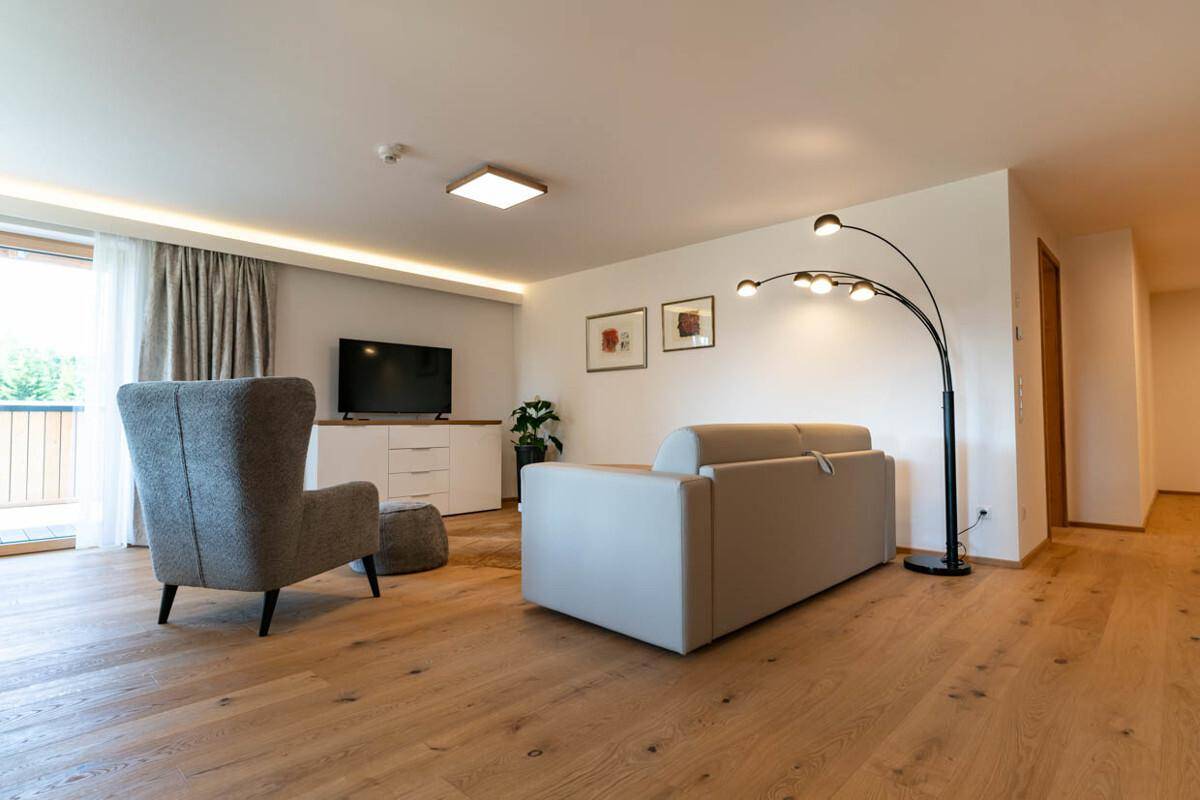 Gemütliches Wohnzimmer mit Sofa, Sessel und Fernseher auf einem weißen Sideboard.