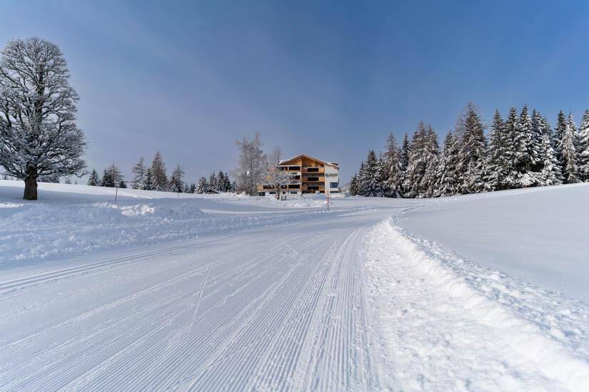 Winterliche Landschaft mit Langlaufloipe und einem modernen Gebäude im Hintergrund.