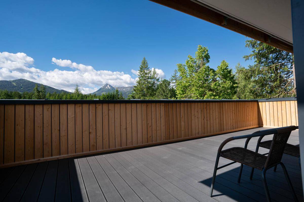 Sonniger Balkon mit Holzboden und weitem Blick auf die umliegende Berglandschaft.