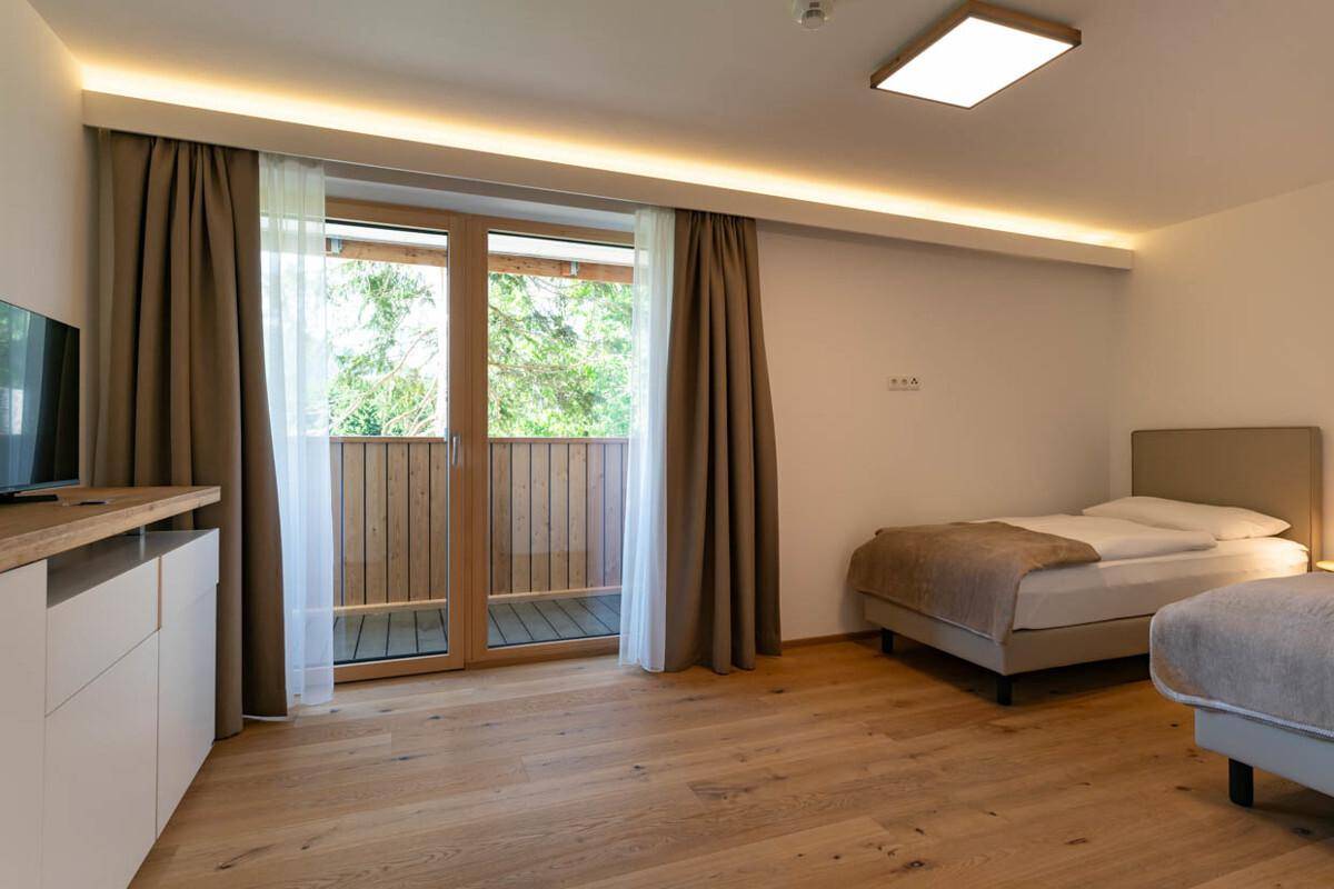 Schlafzimmer mit zwei Einzelbetten, Holzboden und Balkonzugang mit Blick ins Grüne.