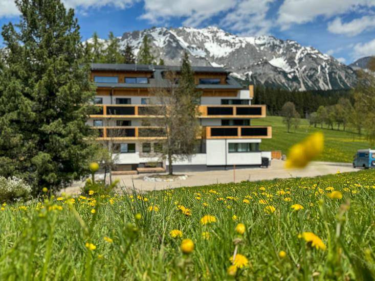 Modernes Gebäude in einer grünen Wiesenlandschaft mit majestätischem Bergblick.