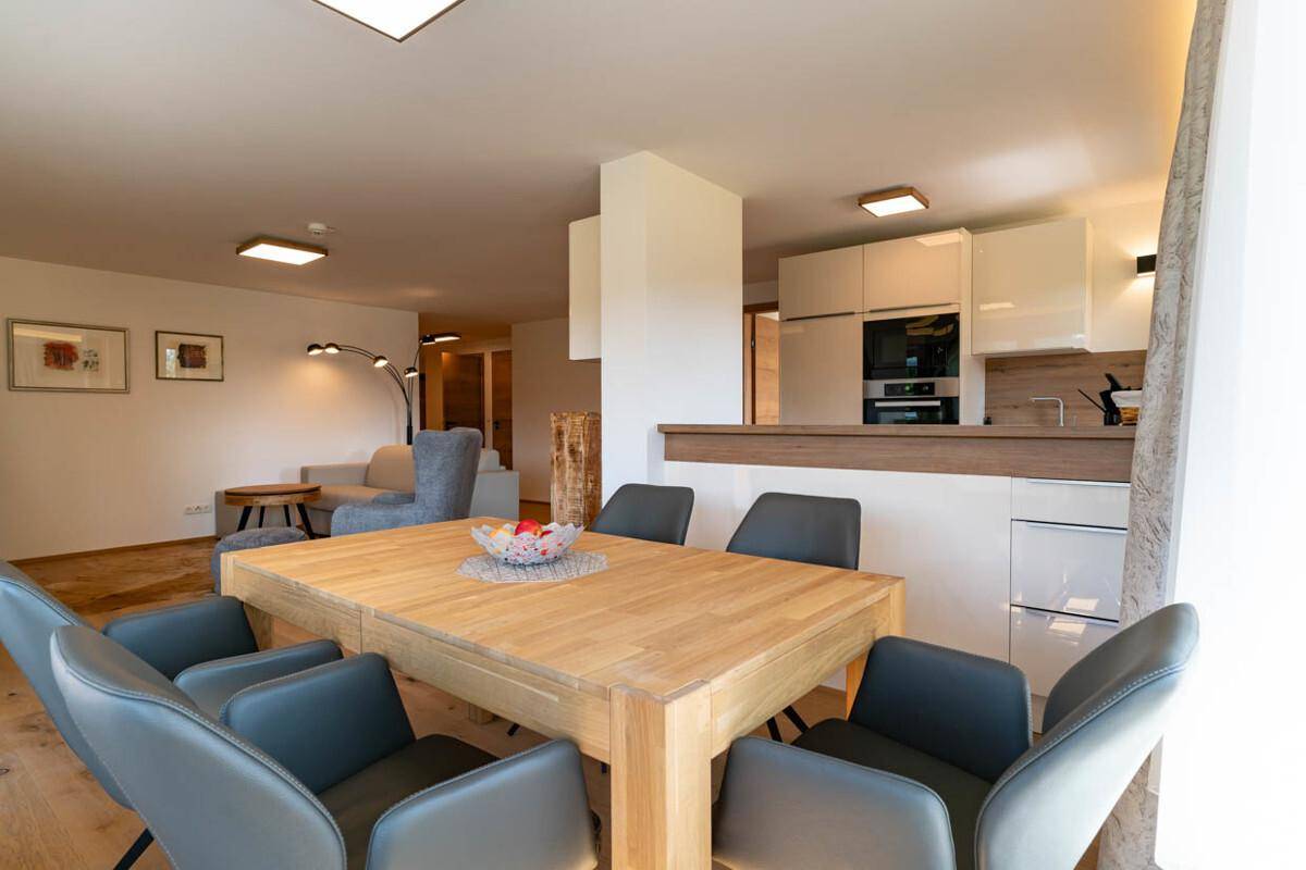 Offener Essbereich mit Holztisch und Blick auf die moderne Küche im Hintergrund.