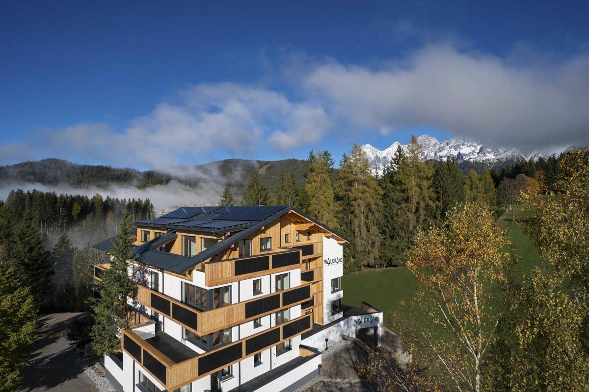 Modernes Gebäude in alpiner Landschaft mit Balkonen und Photovoltaikanlage auf dem Dach.