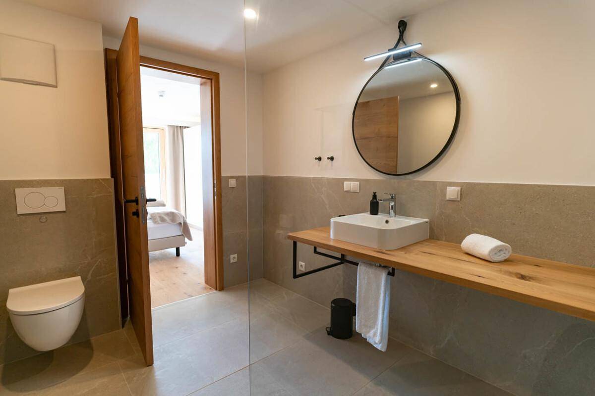 Modernes Badezimmer mit Waschtisch aus Holz, rundem Spiegel und Wand-WC.
