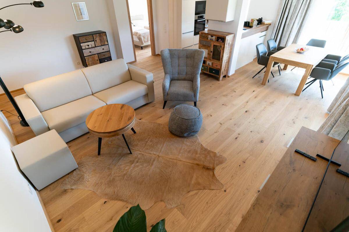 Gemütlicher Wohnbereich mit Holzboden, beigem Sofa und einem dekorativen Kuhfellteppich.