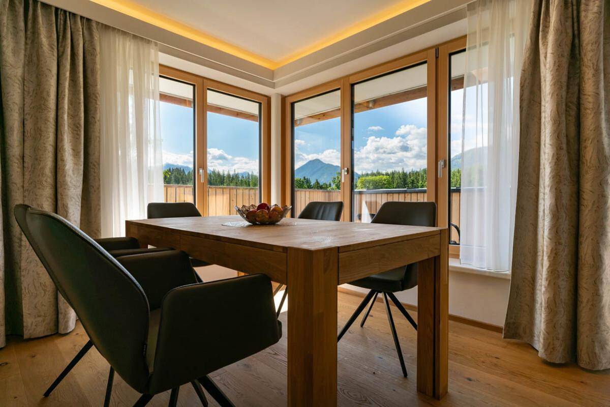 Heller Essbereich mit Holztisch, modernen Stühlen und großen Fenstern mit Bergblick.