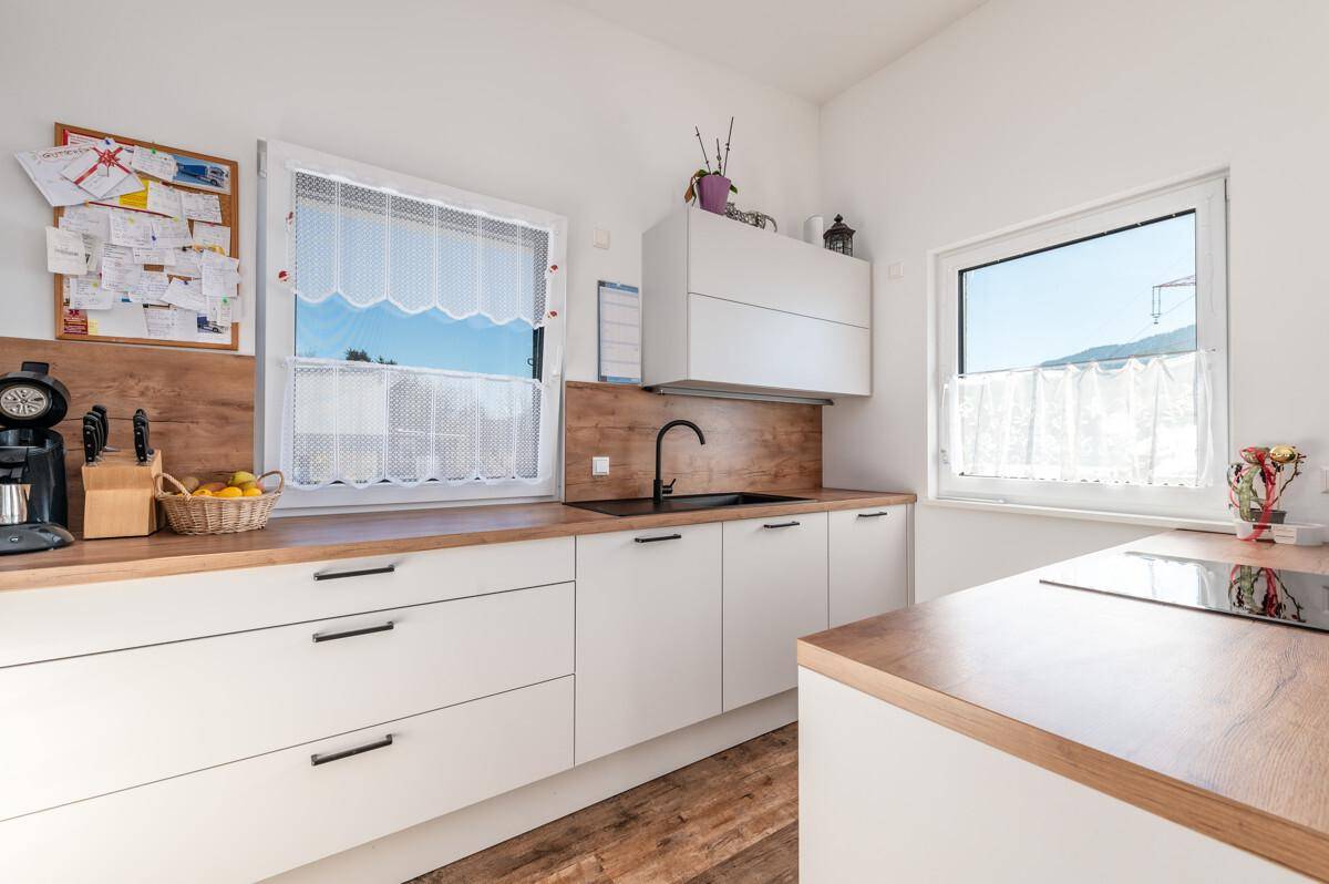 Moderne Küche mit weißen Schränken, Holz-Arbeitsplatten und zwei Fenstern für Tageslicht.