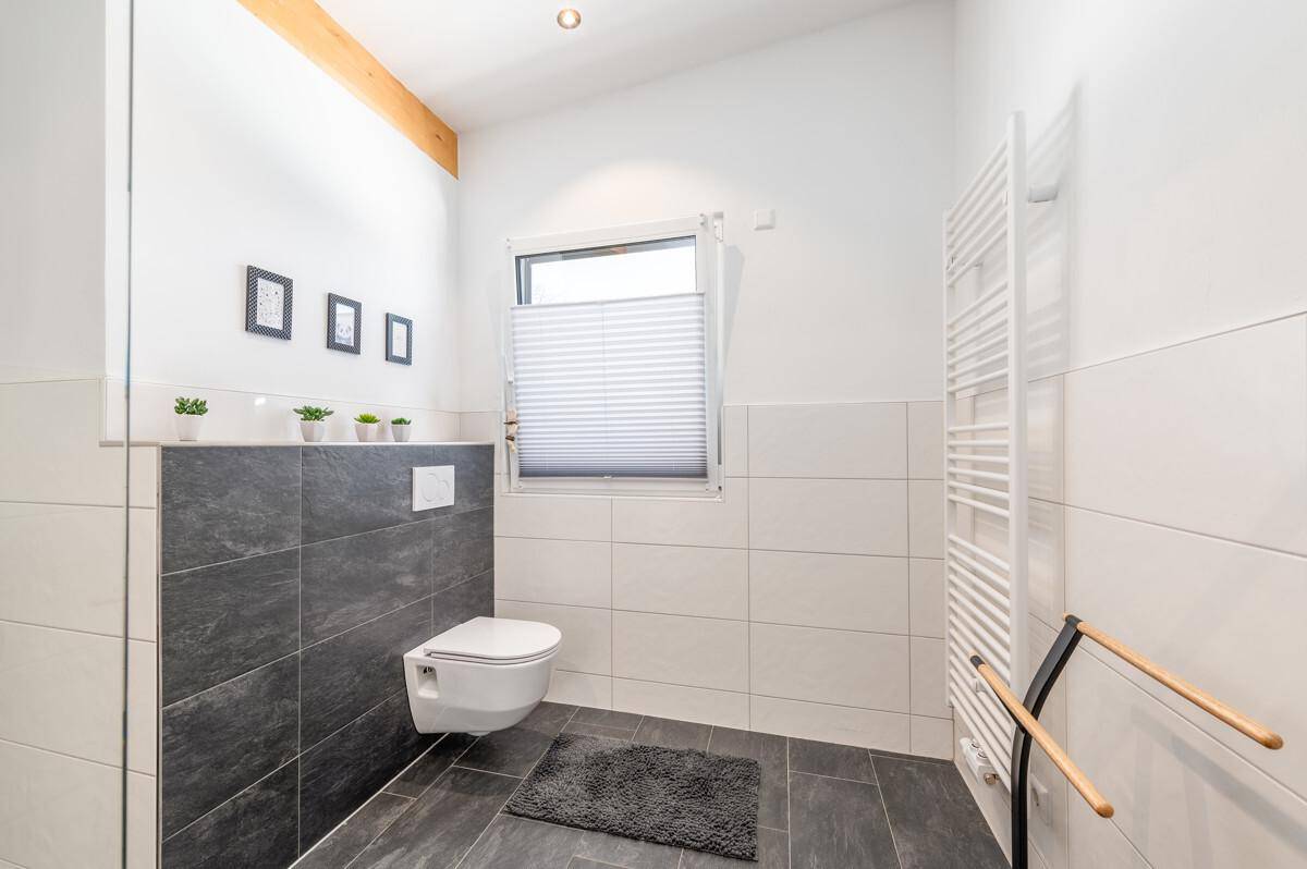 Badezimmer mit wandhängendem WC, Fenster und einem praktischen Handtuchheizkörper.