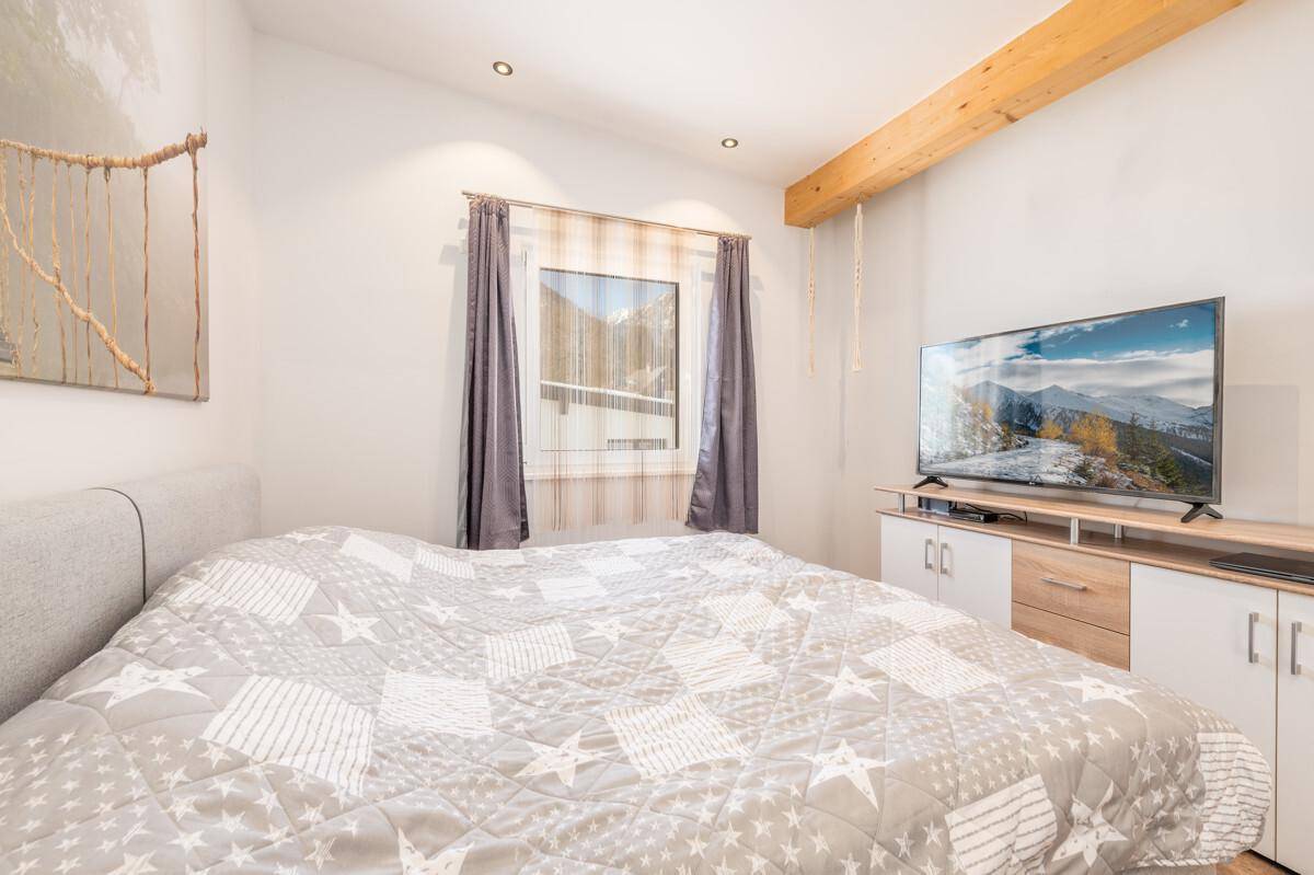 Gemütliches Schlafzimmer mit großem Bett, Fernseher und sichtbarem Holzbalken an der Decke.