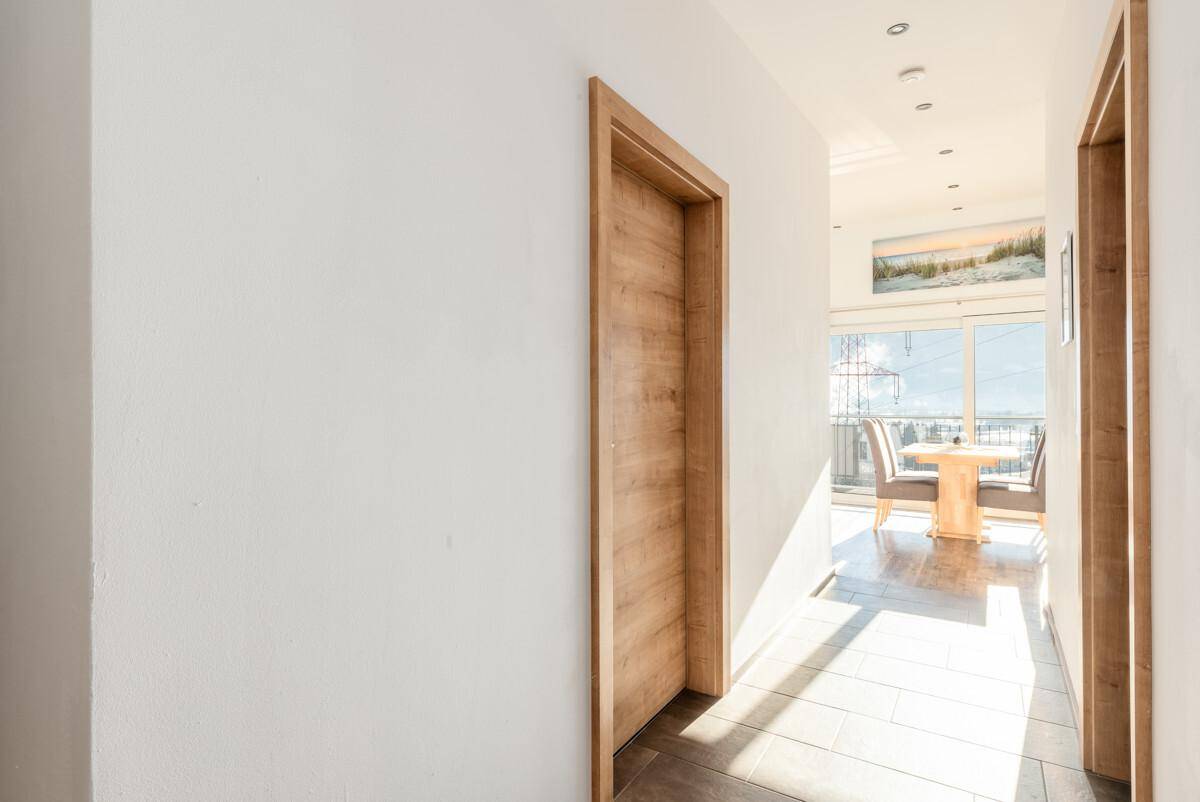 Heller Flur mit Holztüren und viel Tageslicht, der zum Wohnbereich führt.