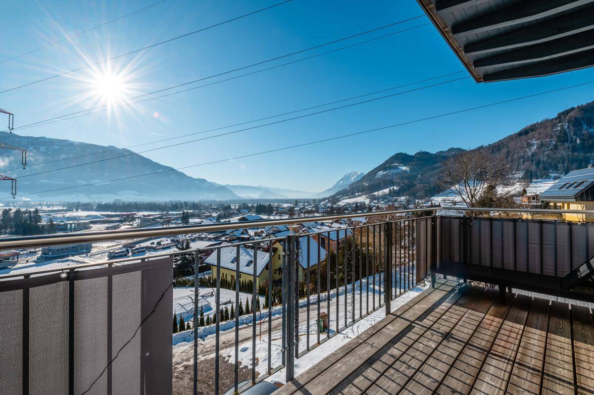 Sonniger Balkon mit Holzboden und weitem Blick über eine verschneite Berglandschaft.